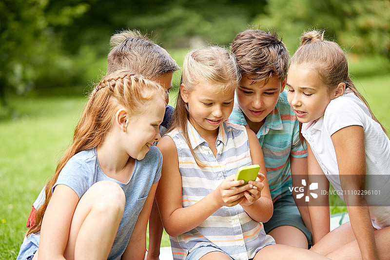 友谊、童年、科技与人：一群快乐的孩子在夏日公园里玩手机图片素材