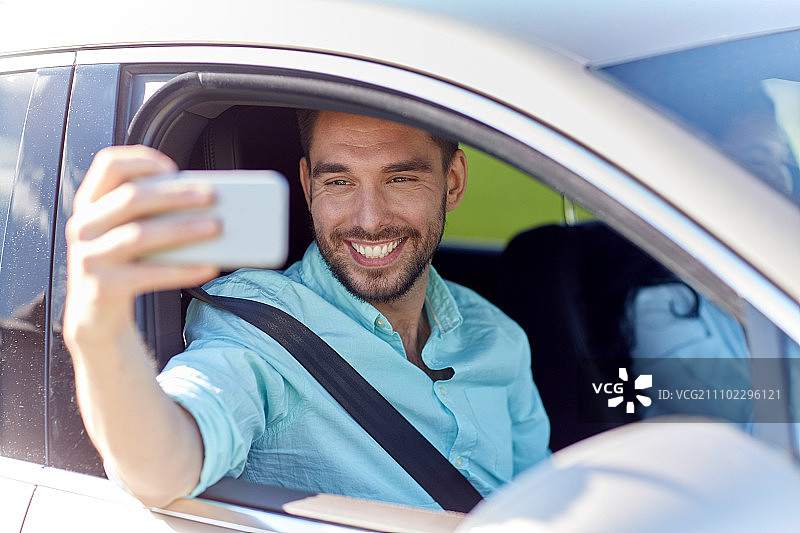 公路旅行，交通，旅行，科技和人物概念 - 快乐的男人在车里用智能手机自拍图片素材