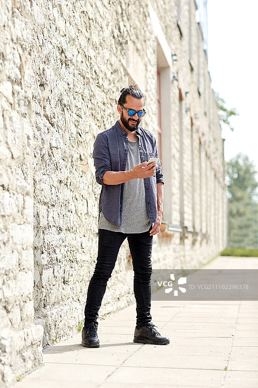 休闲，科技，交流：男子在城市街道石墙上用手机发短信图片素材