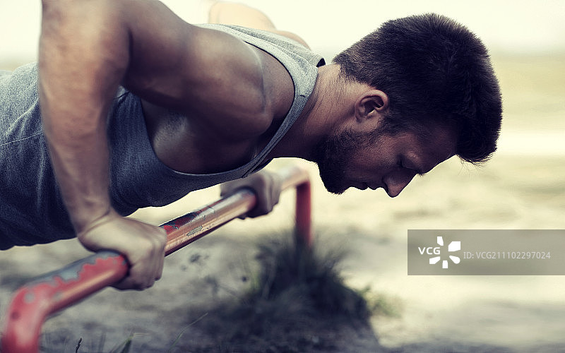 健身运动训练生活方式概念：年轻男子在户外单杠上做俯卧撑图片素材