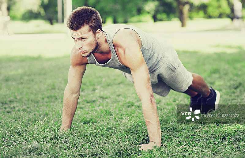 健身运动训练概念：夏季公园草地上做俯卧撑的年轻男人图片素材