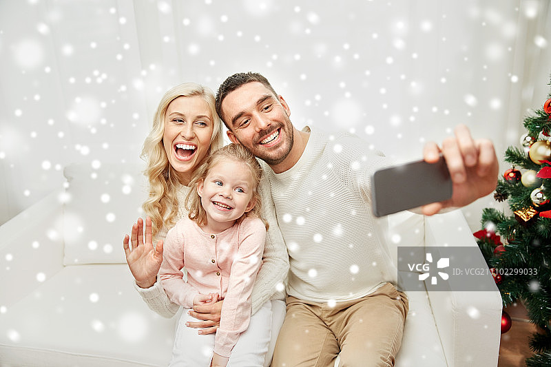 圣诞节，节日，科技概念 - 幸福的家庭坐在沙发上，用智能手机在家自拍图片素材