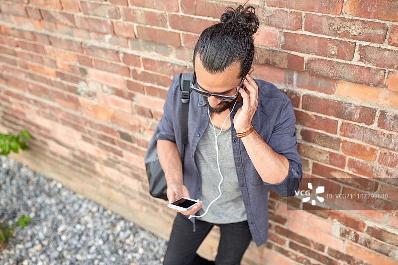 戴耳机、拿智能手机和包的男士在街上听音乐图片素材