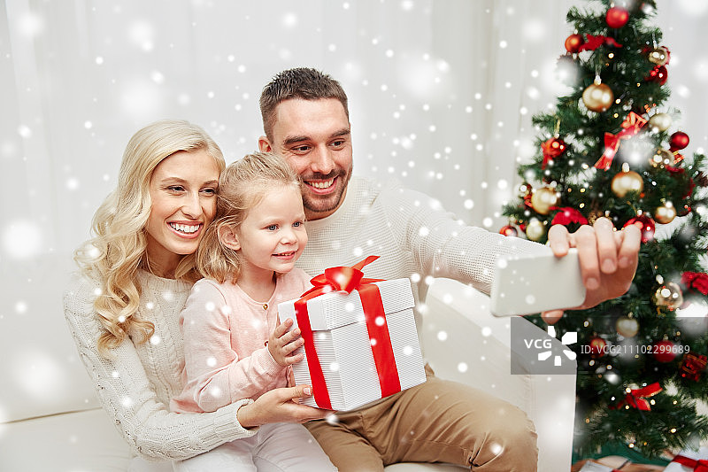 圣诞节，节日，科技概念 - 幸福的家庭坐在沙发上，用智能手机在家自拍图片素材