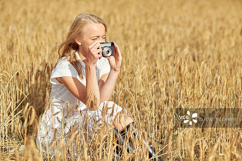 在麦田里用老式胶片相机拍照的年轻女子图片素材