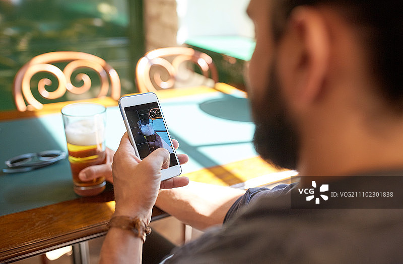 休闲科技概念：男子在酒吧用智能手机拍摄啤酒图片素材