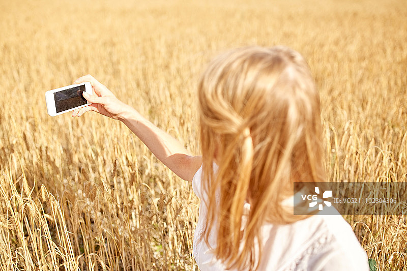 夏日假期：年轻女子用智能手机拍摄麦田图片素材