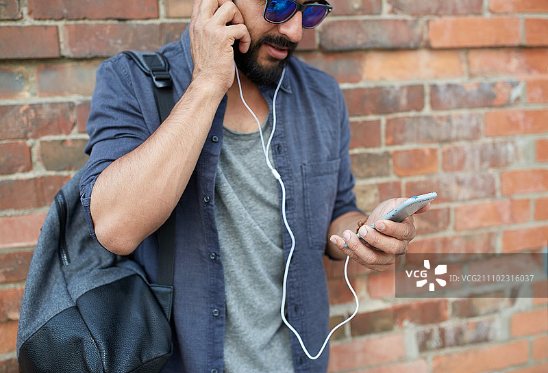 戴耳机、拿智能手机和包的男士在街上听音乐图片素材