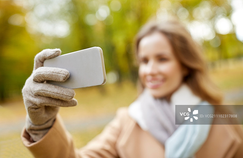 秋季公园里用智能手机自拍的年轻快乐女子图片素材