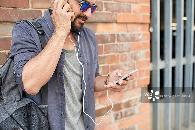 戴耳机、拿智能手机和包的男士在街上听音乐图片素材