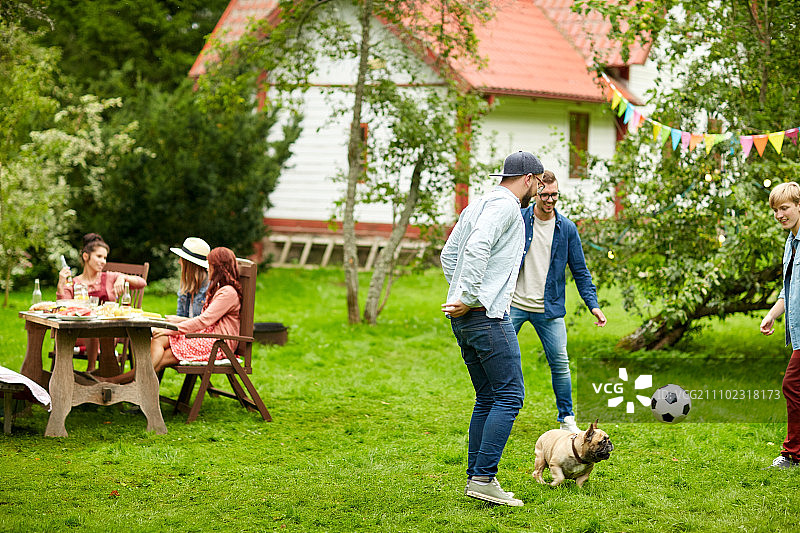休闲假日人们和宠物在夏日花园派对上和狗一起踢足球图片素材