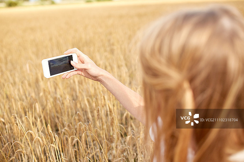夏日假期：年轻女子用智能手机拍摄麦田图片素材