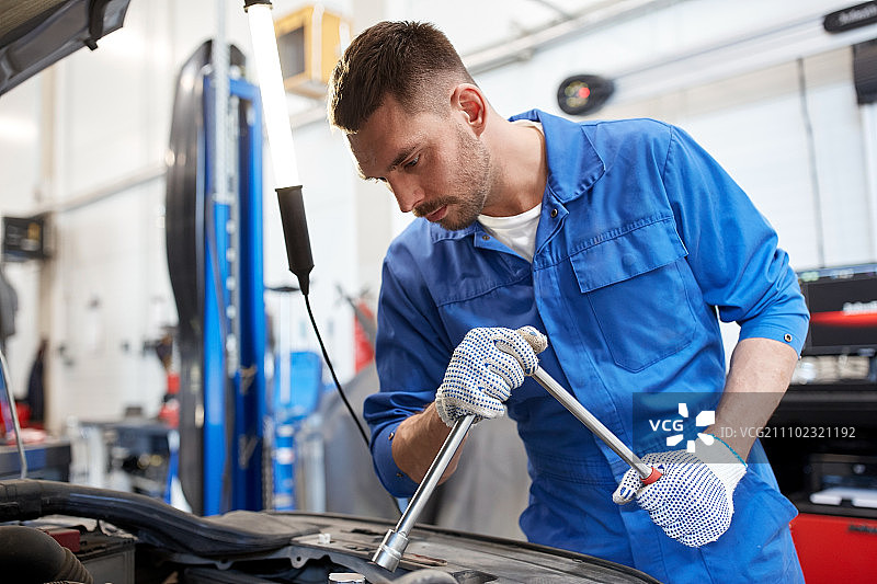 汽车服务、维修、保养概念：汽修工人手持扳手和灯在车间工作图片素材