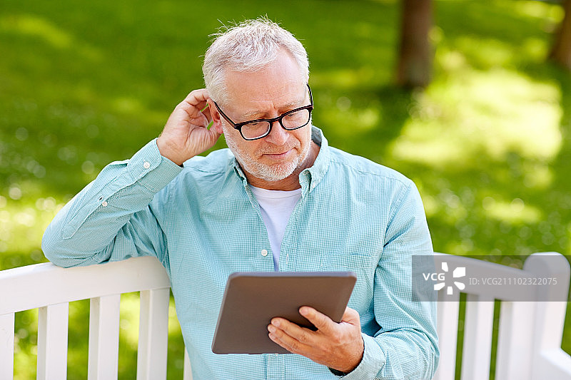 科技、老年人与生活方式、远程学习概念：老人在夏季公园里使用平板电脑图片素材