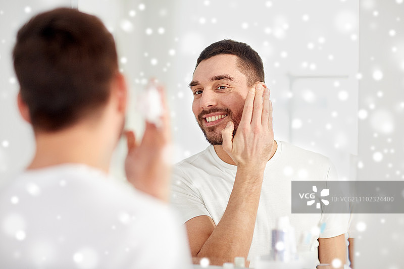 微笑的年轻男人在浴室镜子前涂剃须泡沫图片素材