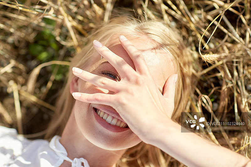 夏季假期：躺在麦田里用手遮住脸的年轻女子图片素材