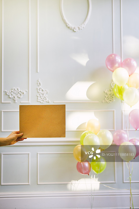 白色墙壁前的彩色氦气球，手拿纸张图片素材