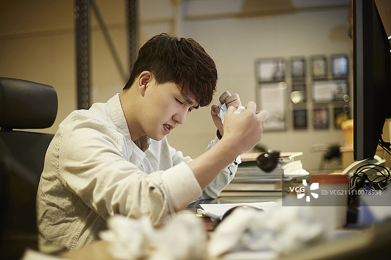 年轻男人坐在堆满皱 पेपर的桌子旁图片素材