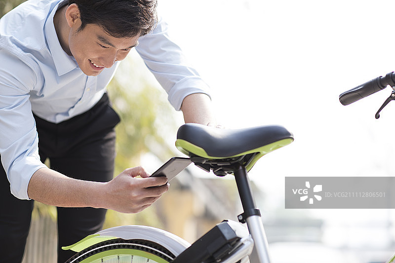 Young Chinese man scanning a QR code to unlock a share bike图片素材