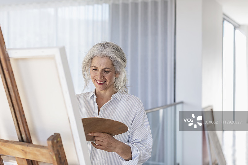 在画架上用调色板绘画的微笑中年妇女图片素材