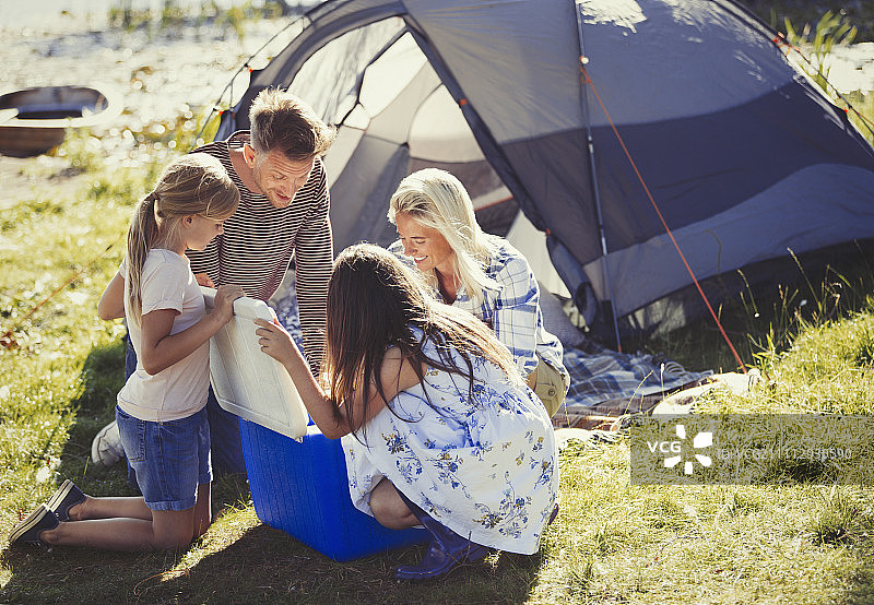 在阳光明媚的露营地帐篷外打开冷藏箱的家庭图片素材