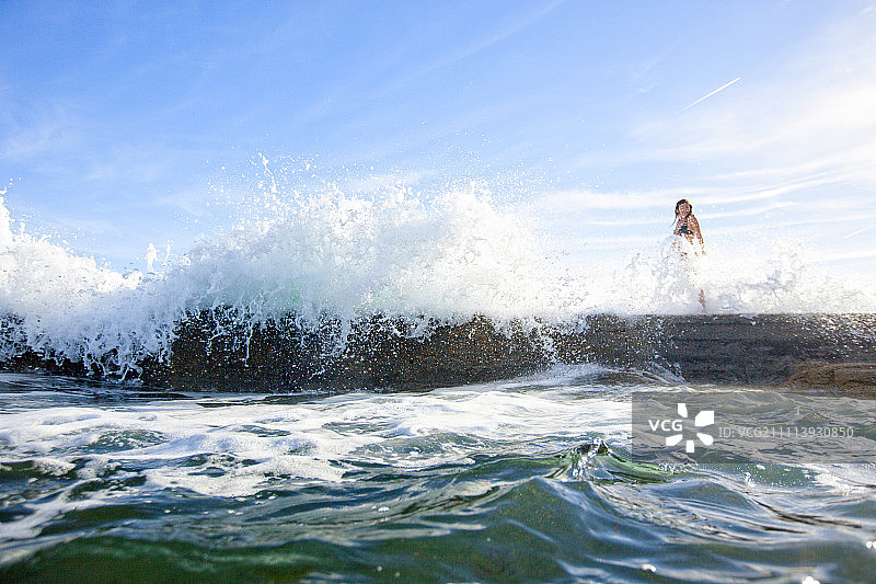 在法国克鲁瓦岛岩石上行走，水花四溅的女人图片素材