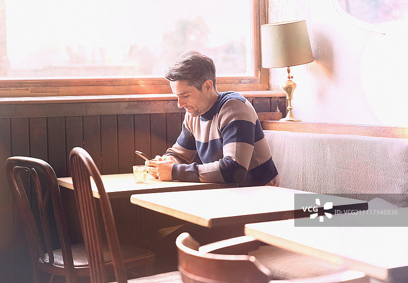 男人在阳光明媚的咖啡馆的桌旁用手机发短信图片素材