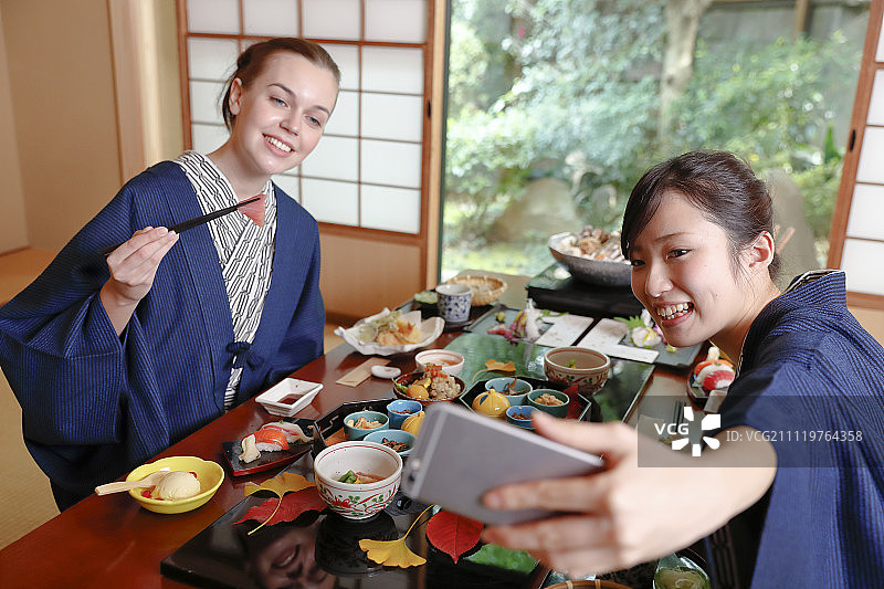 身穿日式浴衣与日本朋友在东京传统日式旅馆用餐的白人女性图片素材