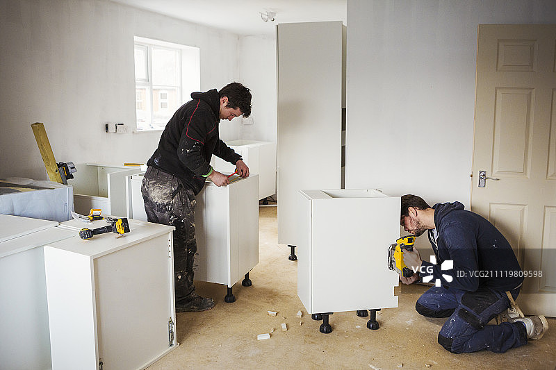 两名建筑工人在建造白色厨房。图片素材