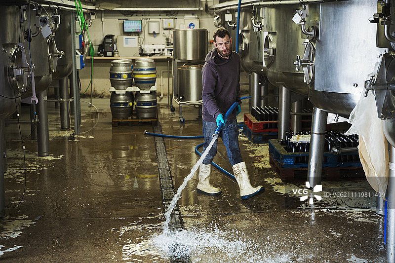 在啤酒厂工作的男子用水管清洗地板。图片素材