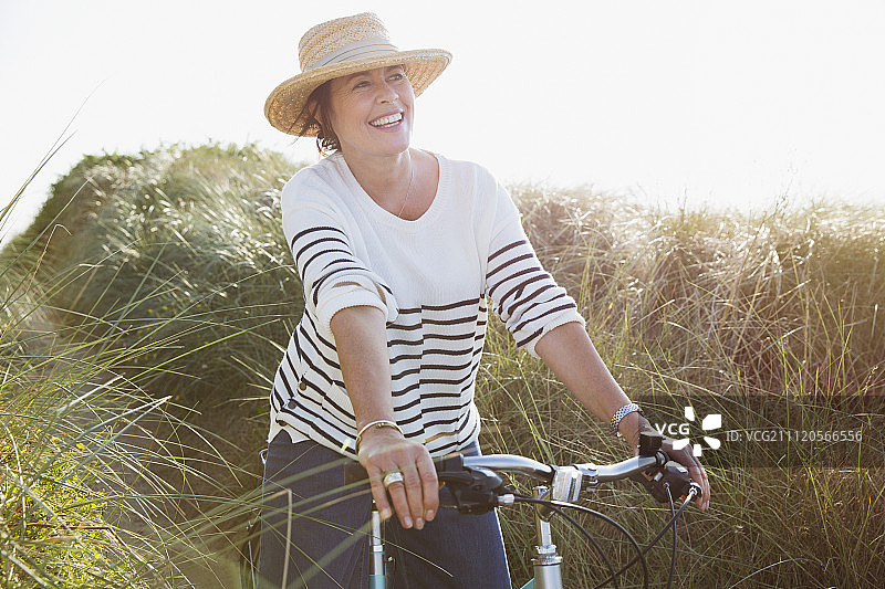 微笑的中年妇女在阳光明媚的海滩草地上骑自行车图片素材