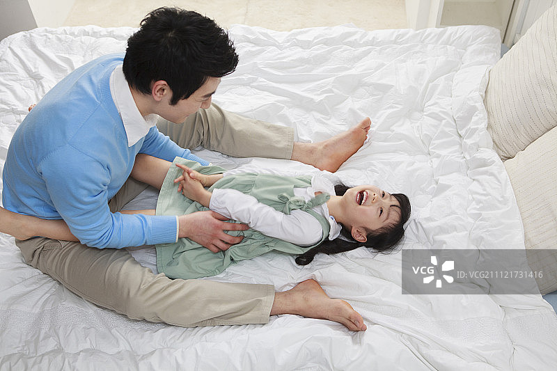 父亲在床上和女儿玩耍，挠她痒痒图片素材