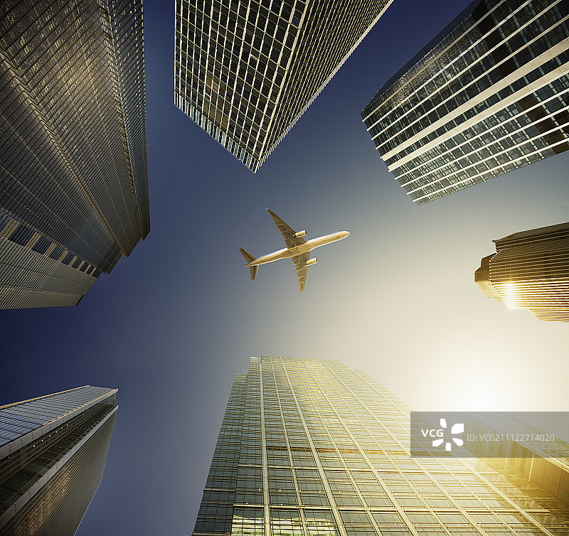 飞机飞过高楼林立的蓝色天空，旅行概念图片素材
