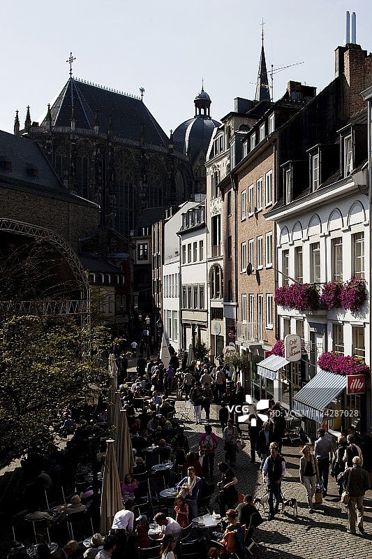 在咖啡馆和街道上行走的人们，背景是德国亚琛大教堂图片素材