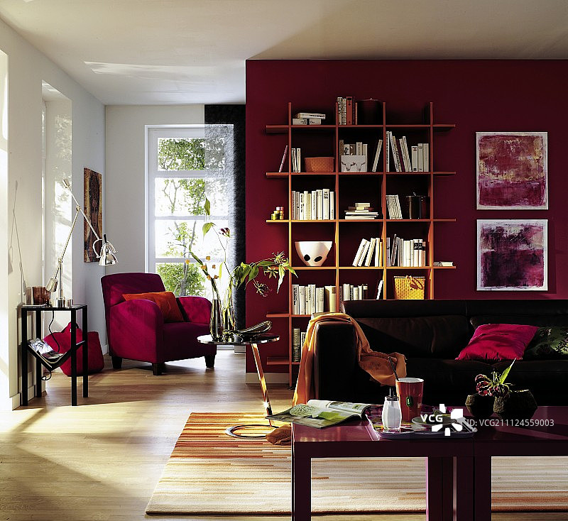 客厅里沙发旁边的边桌、红色扶手椅和书架靠在红墙上图片素材