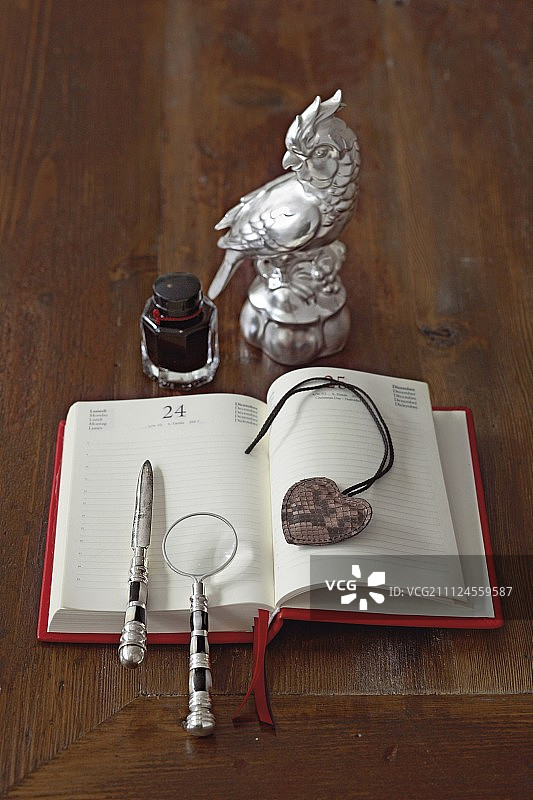 放大镜、开信刀和心形吊坠在带墨水瓶的日记上图片素材