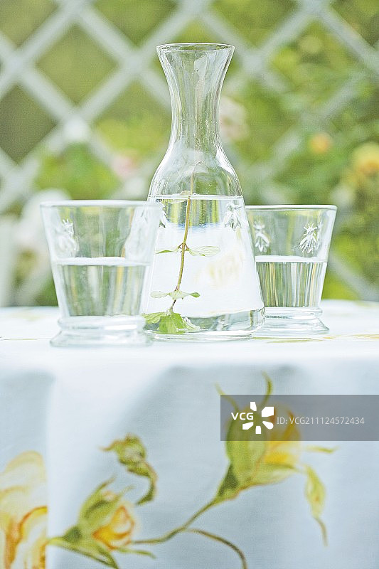 花卉桌布上的玻璃水瓶和两个玻璃杯图片素材