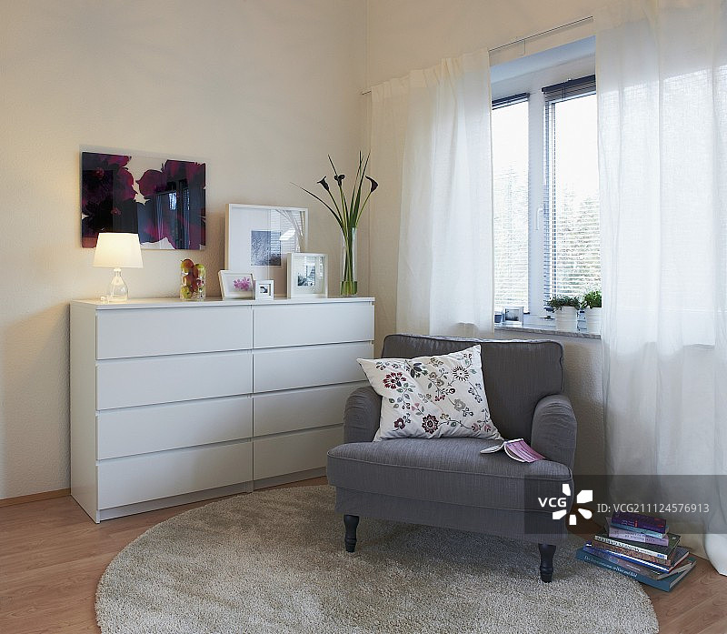 窗前带靠垫的灰色软垫椅子和白色抽屉柜图片素材