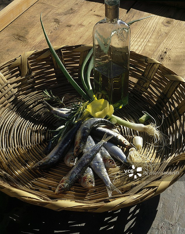 木桌上的一篮沙丁鱼、葱和橄榄油图片素材