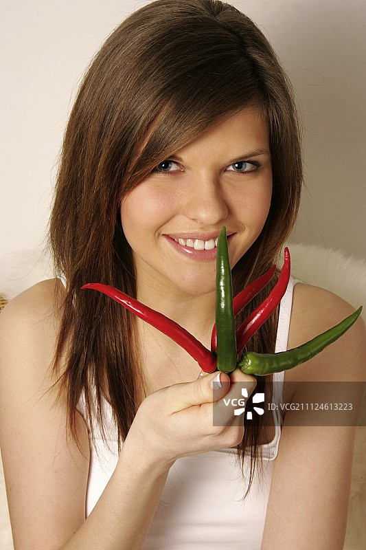 手持红绿辣椒的棕发微笑女子肖像图片素材