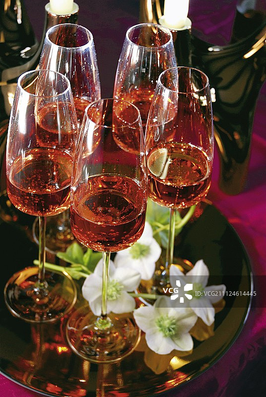 装在玻璃杯里、放在白色盘子上的玫瑰香槟与铁筷子图片素材