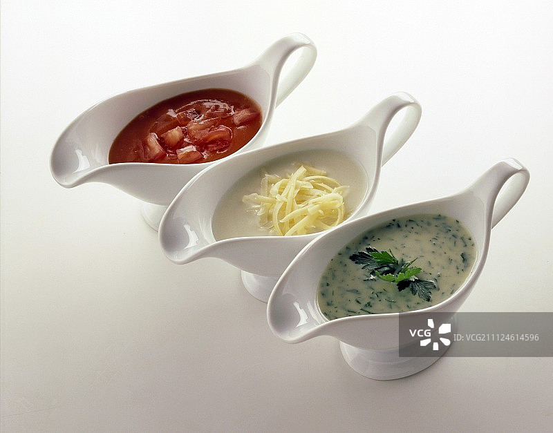 白色背景下酱汁船中的番茄酱、奶酪酱和香草酱图片素材