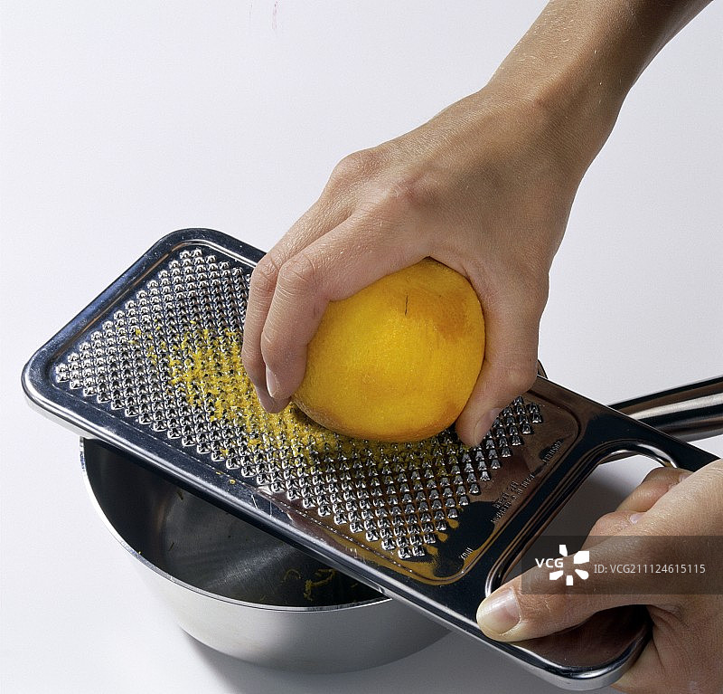 用磨碎器剥橙子皮的手部特写图片素材