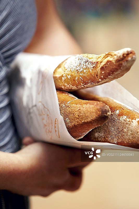 在法国，女人手臂下夹着三根法棍面包特写图片素材