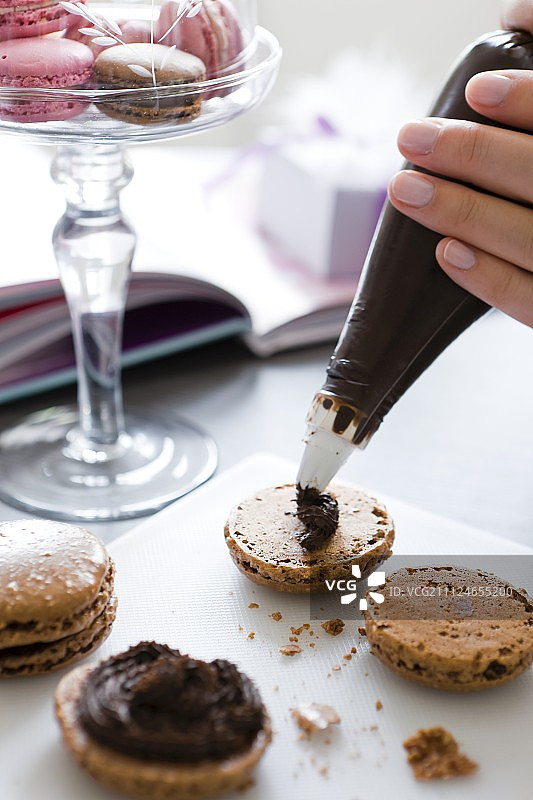 用裱花袋将巧克力奶油填充到一半的马卡龙中图片素材