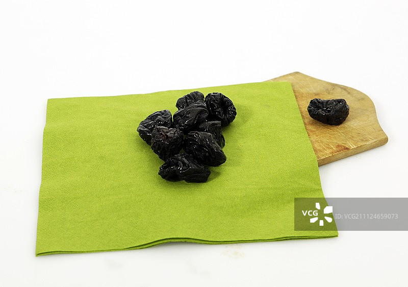 白色背景下，绿布和木盘上的干梅子图片素材