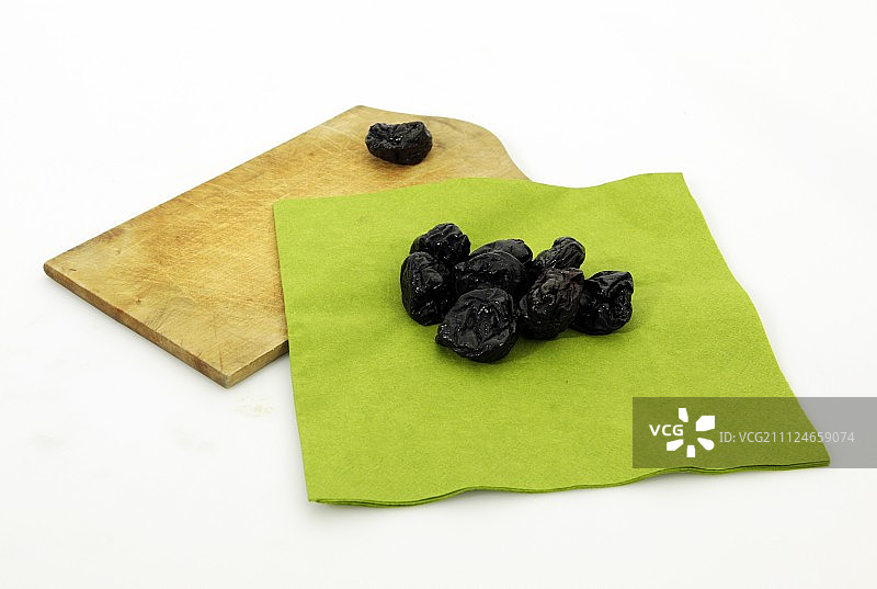 白色背景下，绿布和木盘上的干梅子图片素材