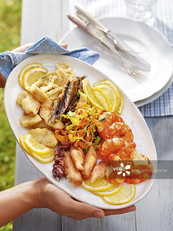 手持盘中炸鱼和海鲜特写图片素材
