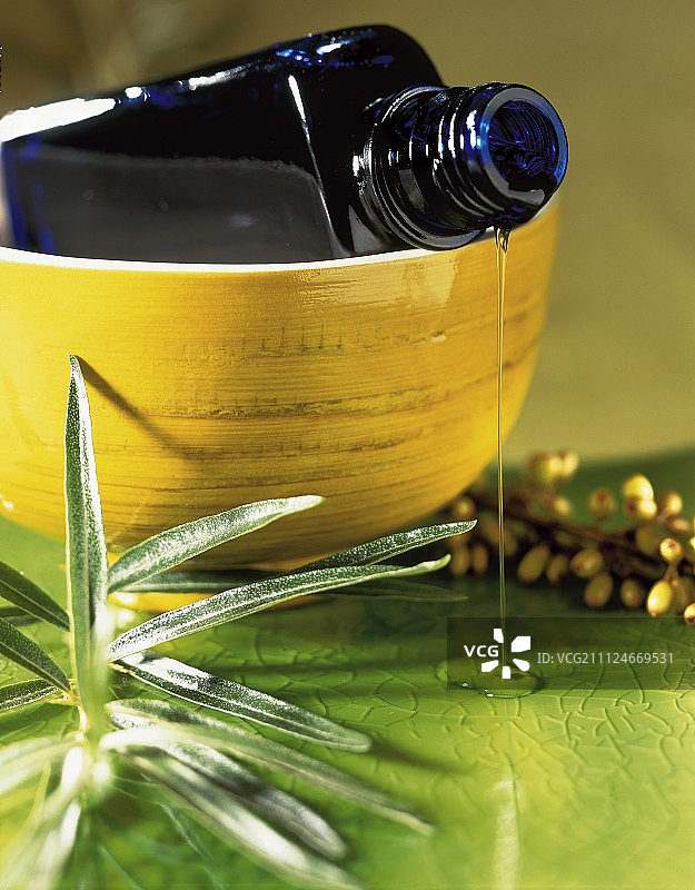 从蓝色瓶中流出的沙棘油，置于黄色碗中图片素材