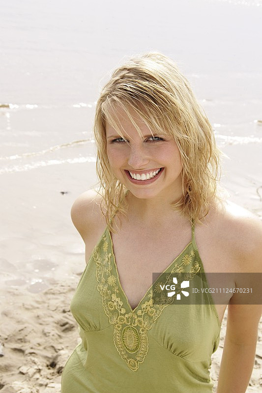 在海滩上微笑的金发美女肖像，身穿绿色吊带衫图片素材